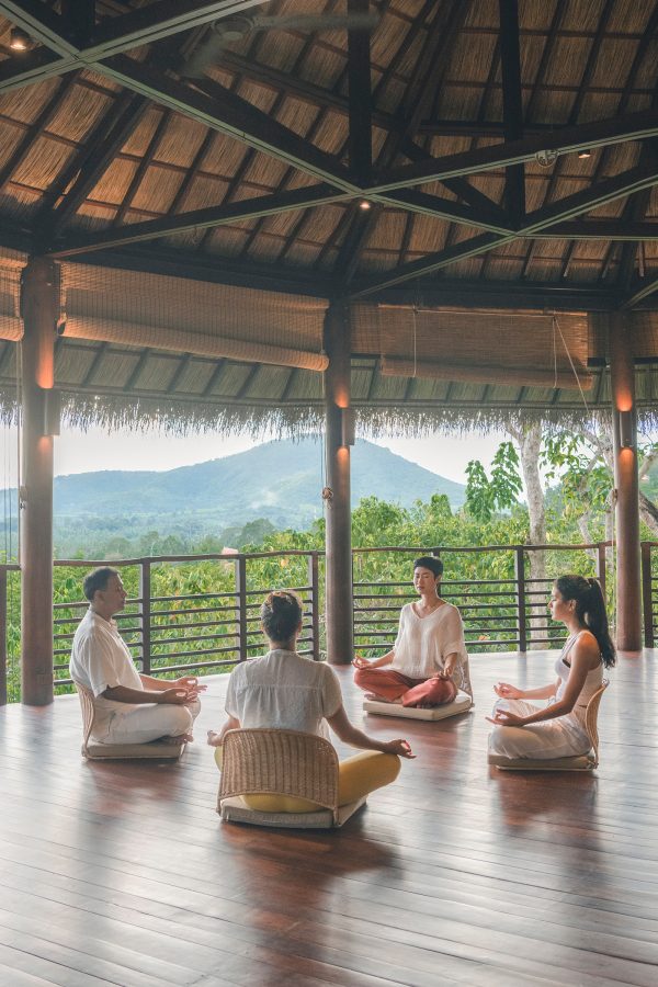 Four people sitting in a circle with their legs crossed during a group meditation at Kamalaya, Koh Samui, in the daytime.