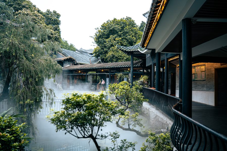 Exterior of Panxi Restaurant, featuring a traditional courtyard filled with plants and trees and shrouded in mist. 