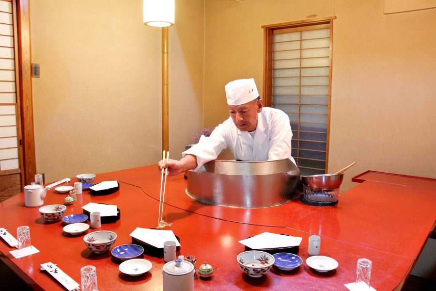 Chef reaches across the counter with long chopsticks at Tempura Tenko in Tokyo.
