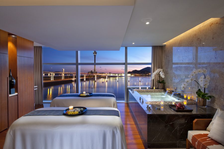 A spa room in Macao’s Mandarin Oriental has a hot tub, two beds and a view over the HZMB Bridge and the Macao tower in the evening.
