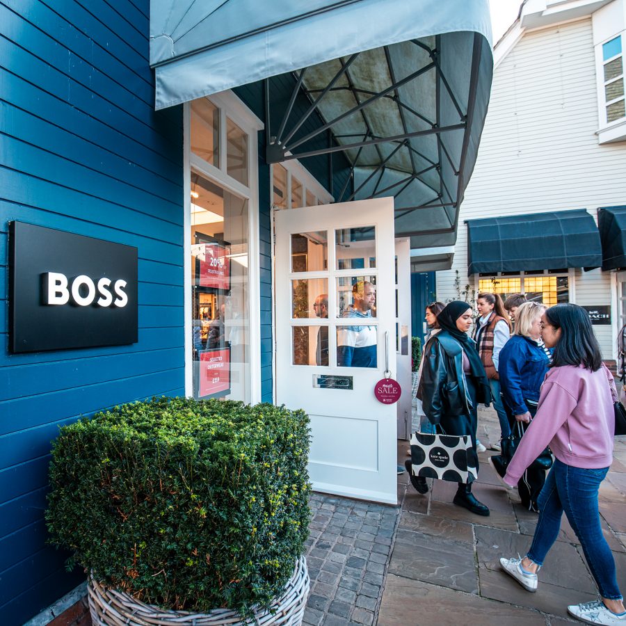 The logo of Boss is on display outside its shop at Bicester Village, as several shoppers enter and exit.