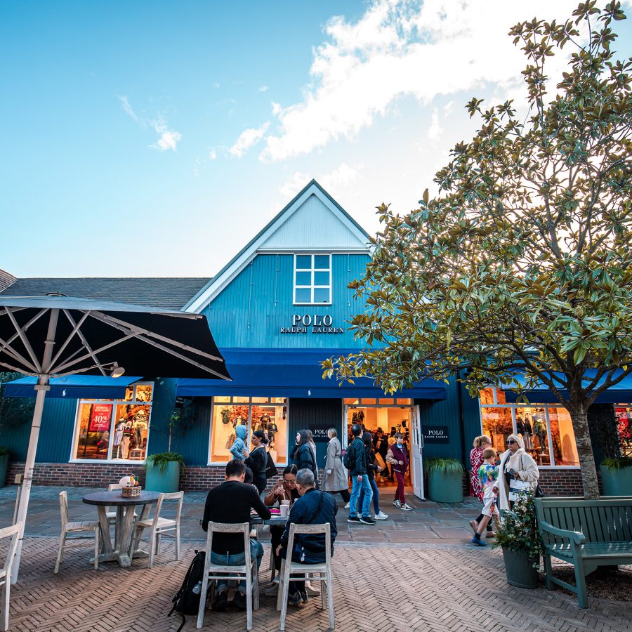 Polo Ralph Lauren’s exterior is a blue house-like structure and is near seating for shoppers. 