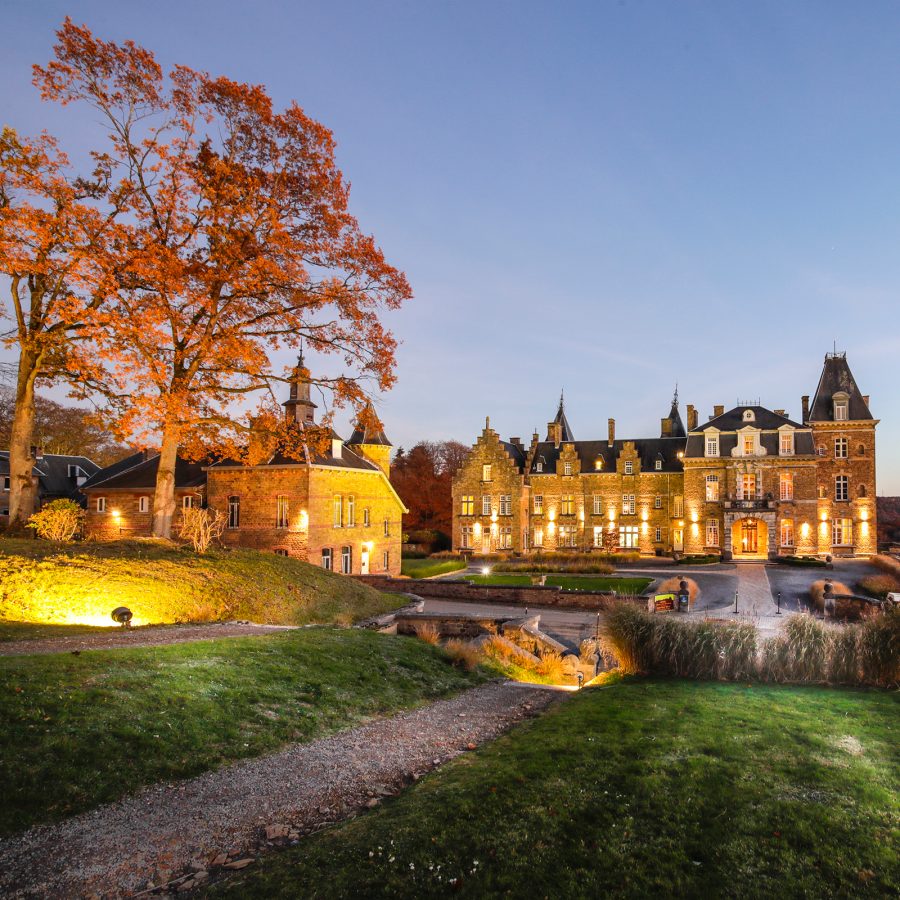 The illuminated Domaine de Ronchinne hotel at twilight in Belgium.