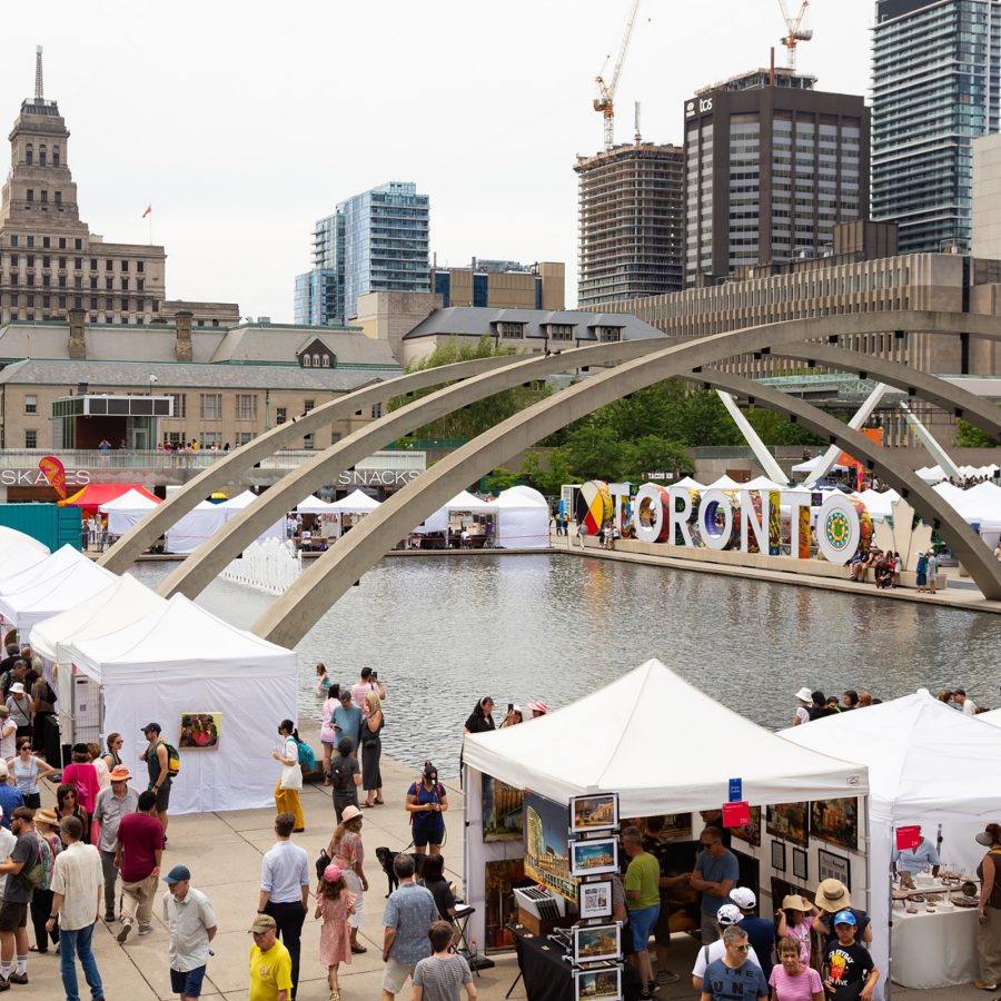Exterior view of visitors and spectators milling around the booths in downtown Toronto at the Toronto Outdoor Art Fair.