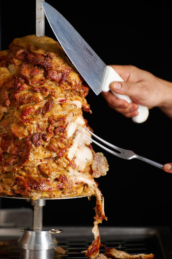 Hands holding a fork and knife slicing halal meat off a vertical rotisserie for doner kebab at Cafe Kool at Kowloon Shangri-La, Hong Kong.