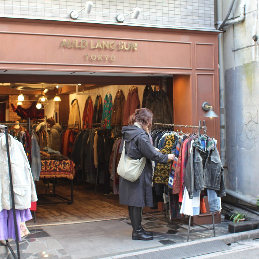 A woman browses a rack of jackets at Auld Lang Syne, Tokyo, in the daytime.