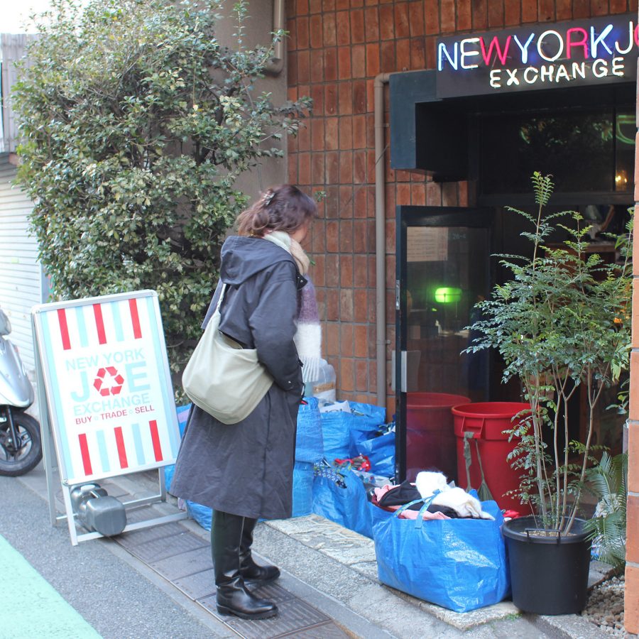 A woman in a black coat stands in front of the entrance to New York Joe Exchange in Tokyo in the daytime.