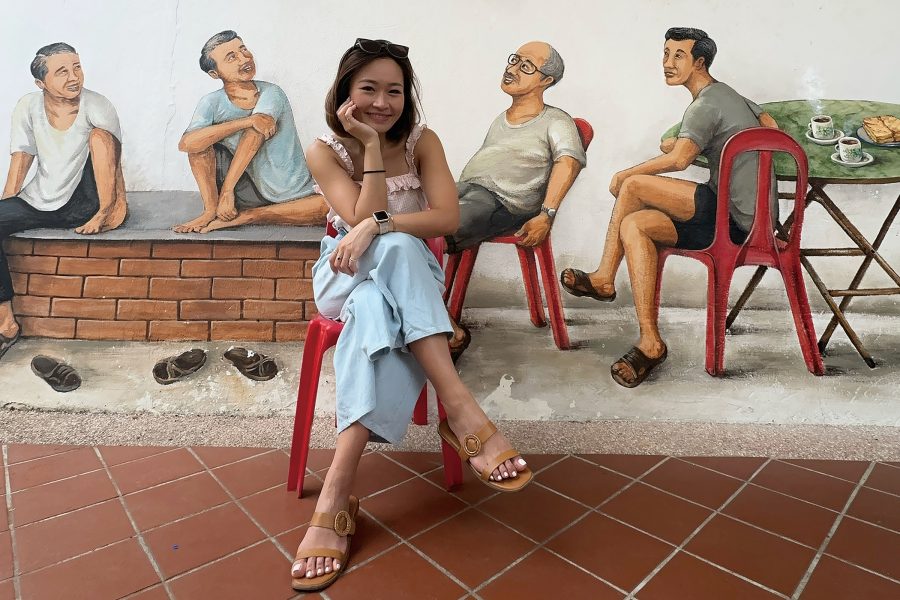 Cathay Pacific crew member Charlie Chan smiles as she sits on an outdoor chair in front of a mural in Tiong Bahru, Singapore