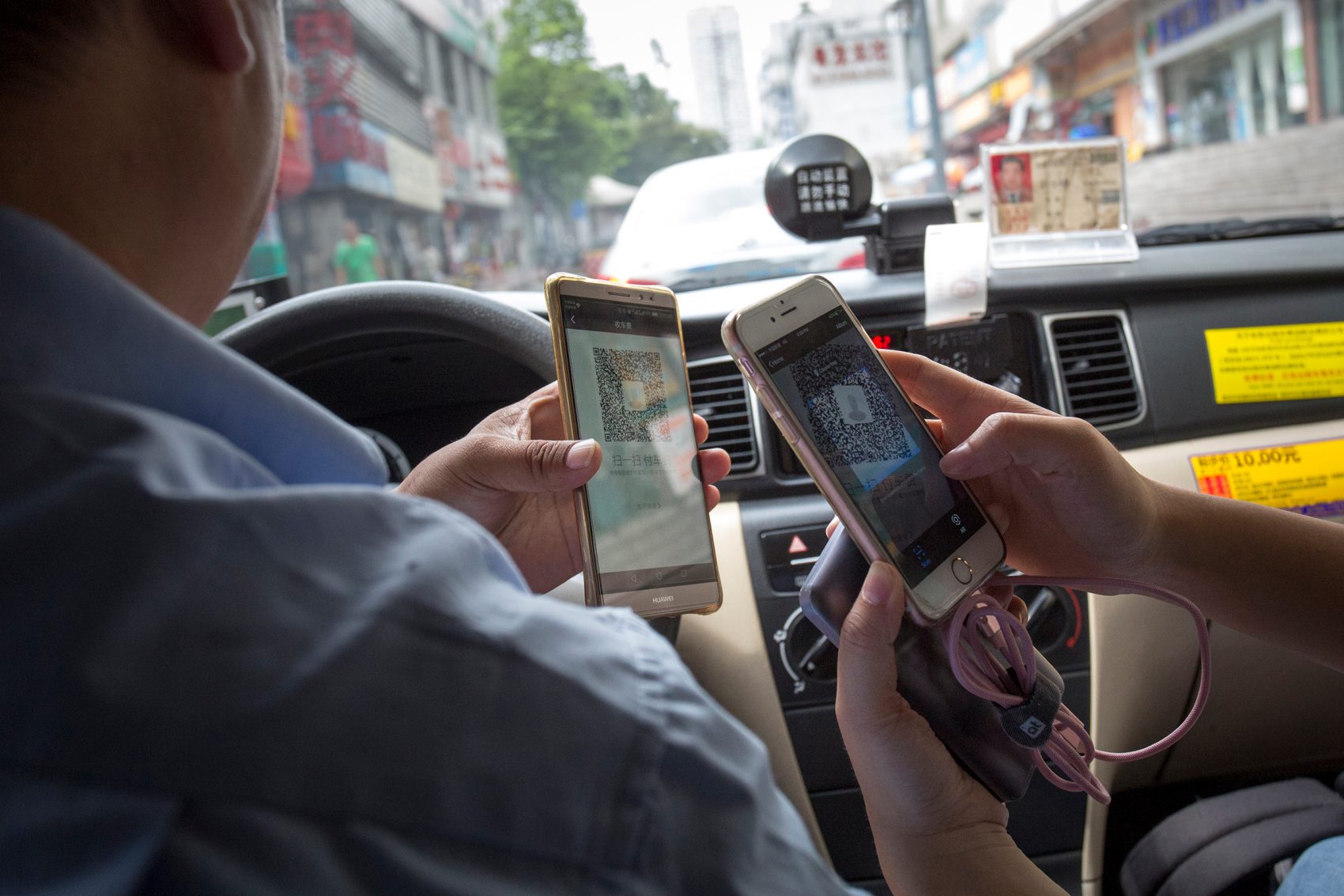 A driver and a passenger use their phones and QR codes to perform a transaction.