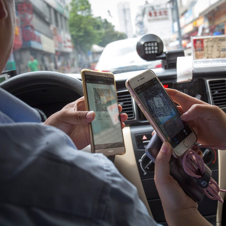 A driver and a passenger use their phones and QR codes to perform a transaction.