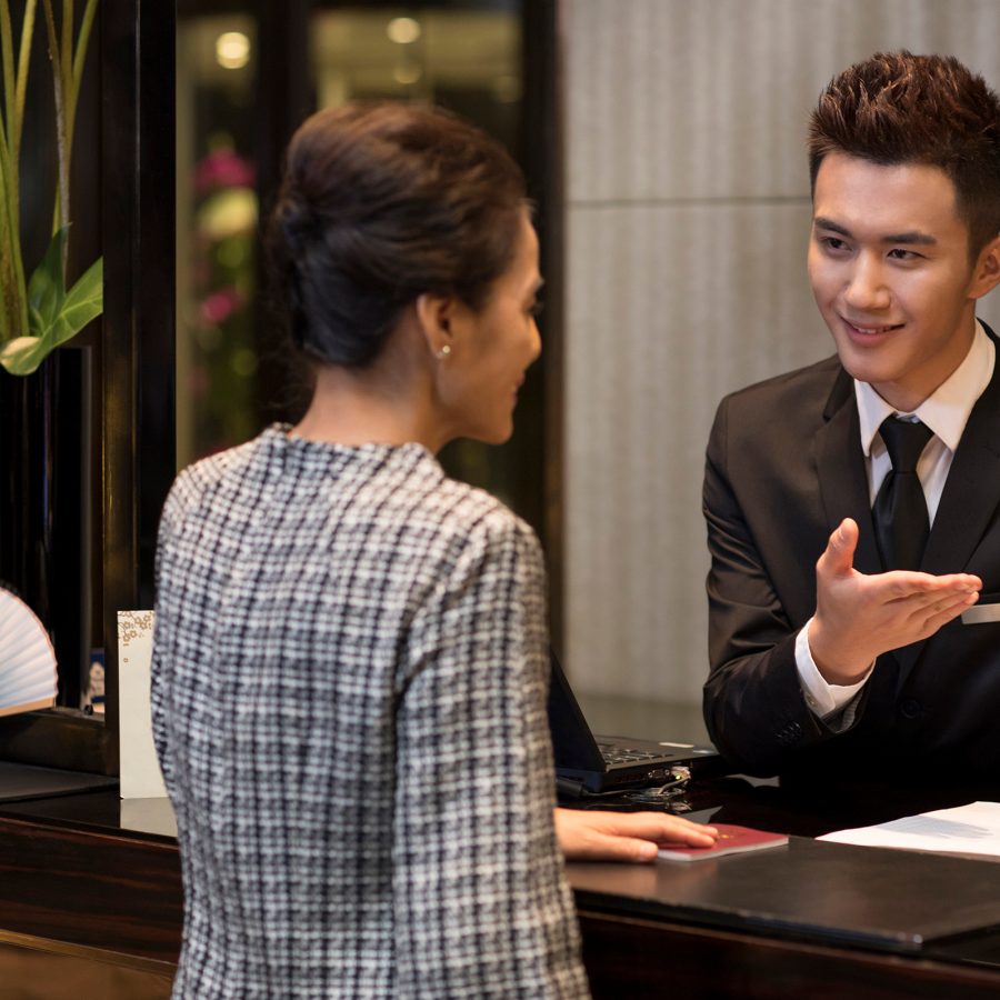 A man behind a cashier gestures to something on his phone to a customer.
