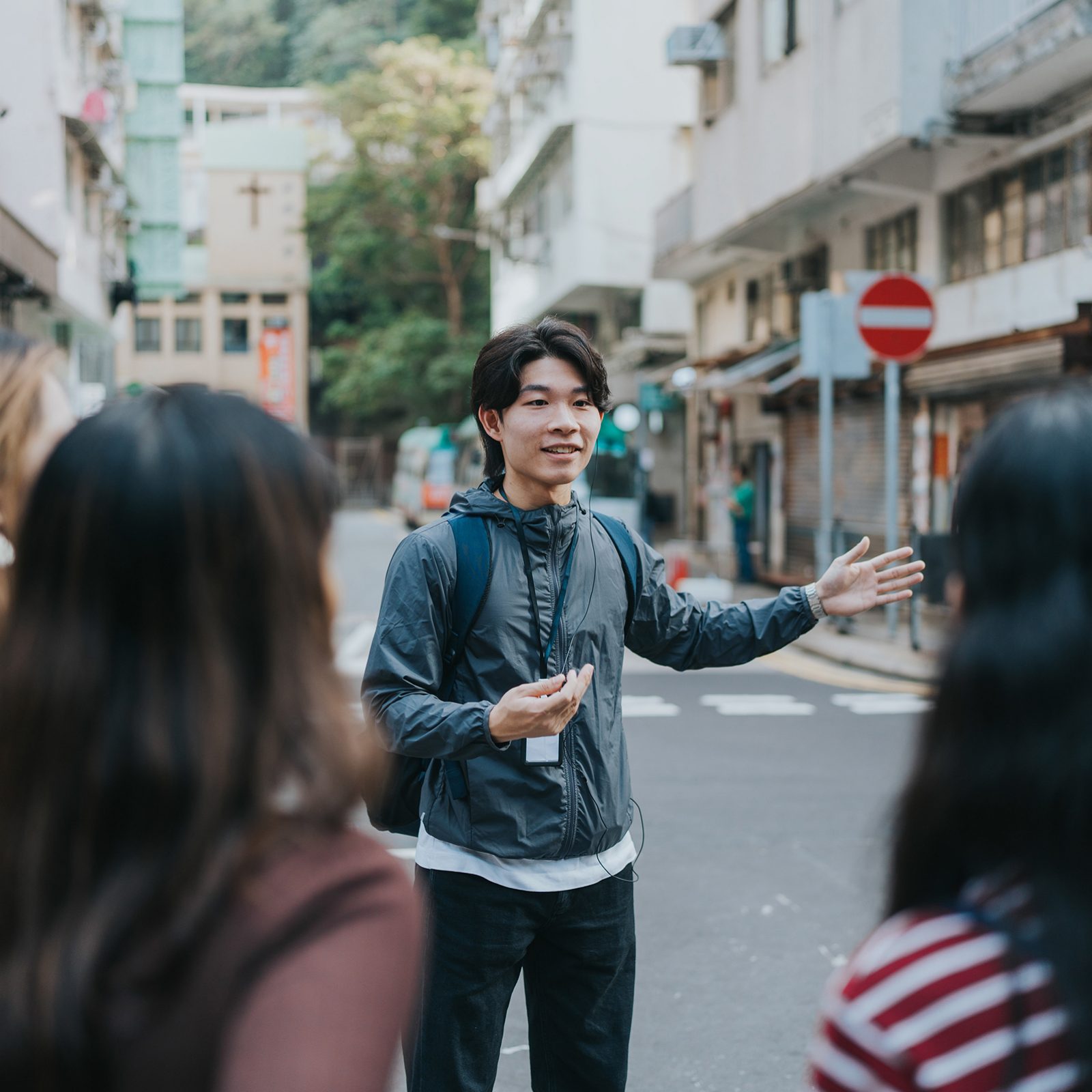 A tour guide talks to a group of travellers and gestures in the middle of a street.