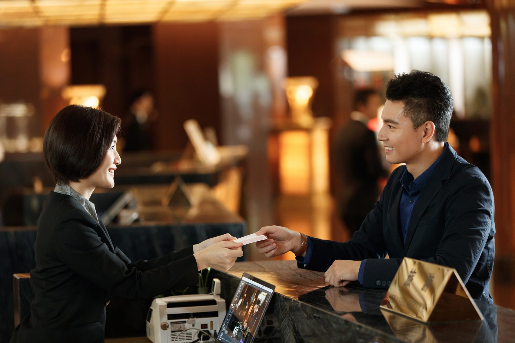 A man smiles as he hands a woman at a counter money to pay for a service.