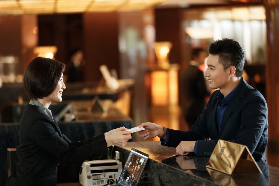 A man smiles as he hands a woman at a counter money to pay for a service.