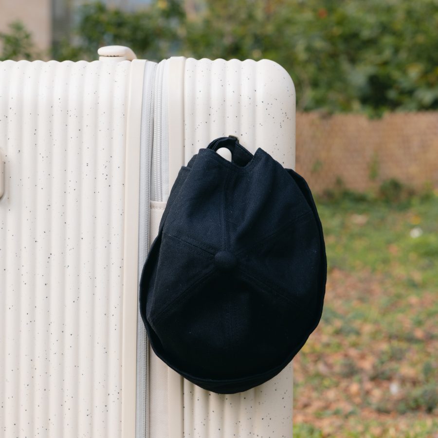 Close-up of a black cap hanging on an exterior hook of the ivory Samsonite TOIIS XP Trunk. 