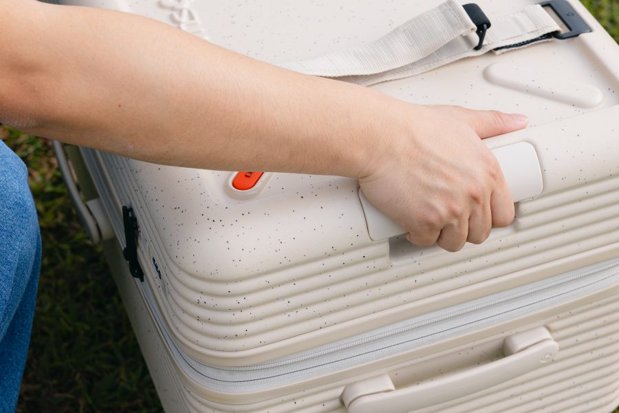 Close-up of a hand holding on to a large groove at the top of the ivory Samsonite TOIIS XP Trunk. 