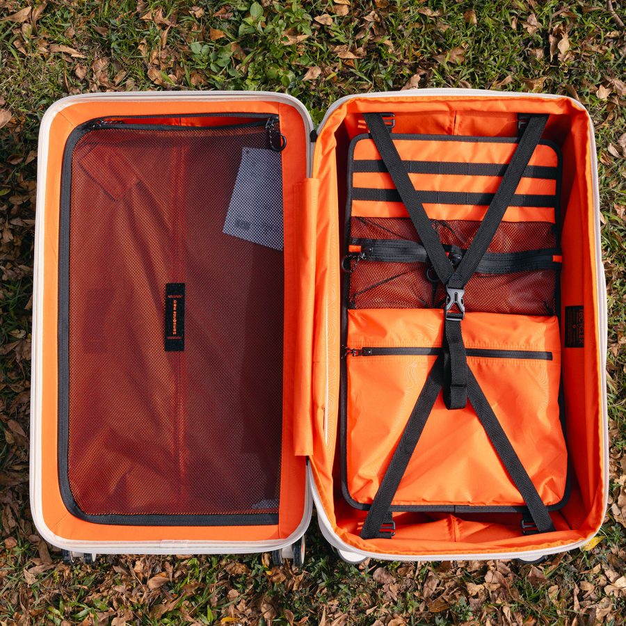 The Samsonite TOIIS XP Trunk on a grassy field, unzipped to reveal its orange interiors.