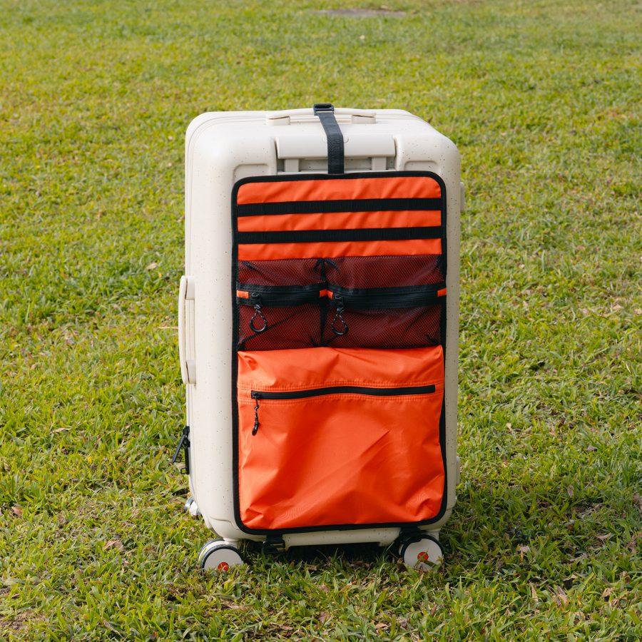 The Samsonite TOIIS XP Trunk on a grassy field, with its orange organiser hanging from the front of the case.