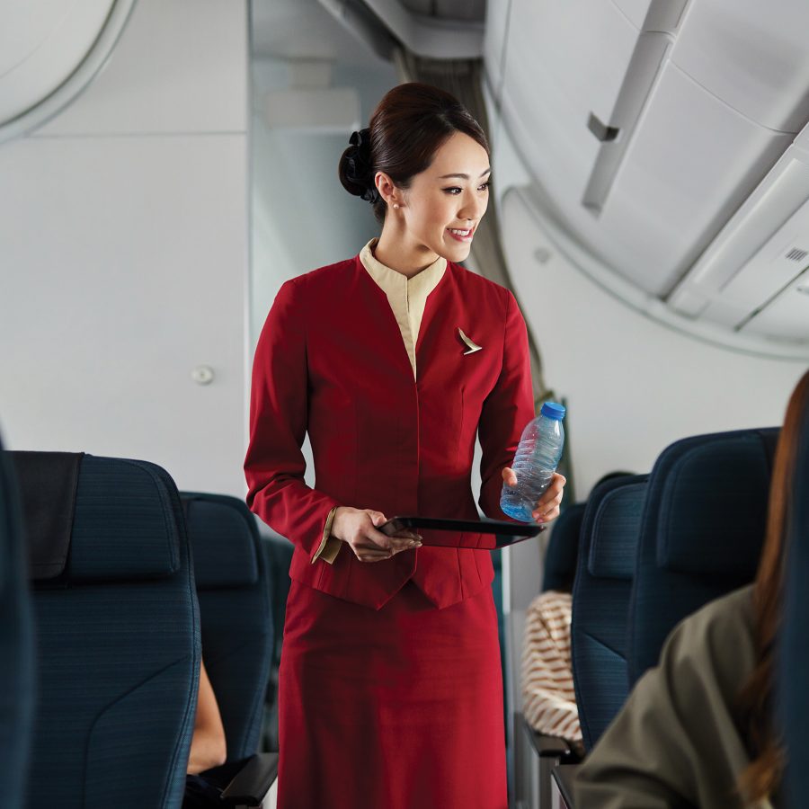 A female Cathay Pacific cabin crew handing out a plastic bottle of water to a passenger inflight.
