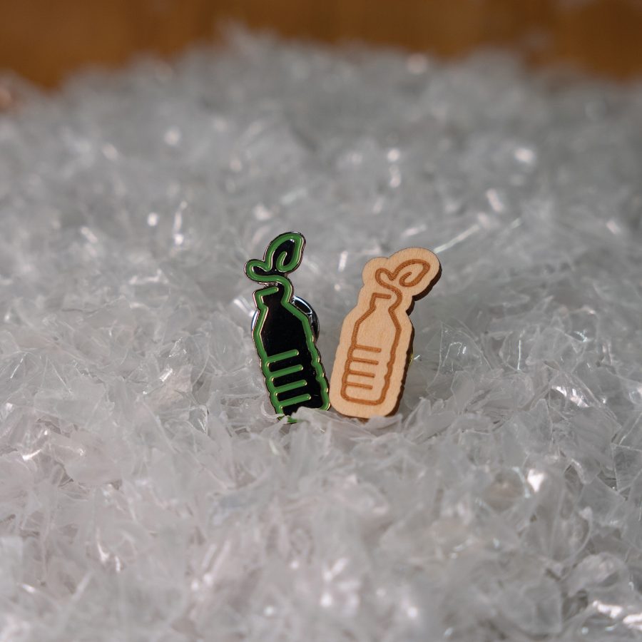 New Life Plastics pins in the shape of water bottles. One is green, the other is brown. 