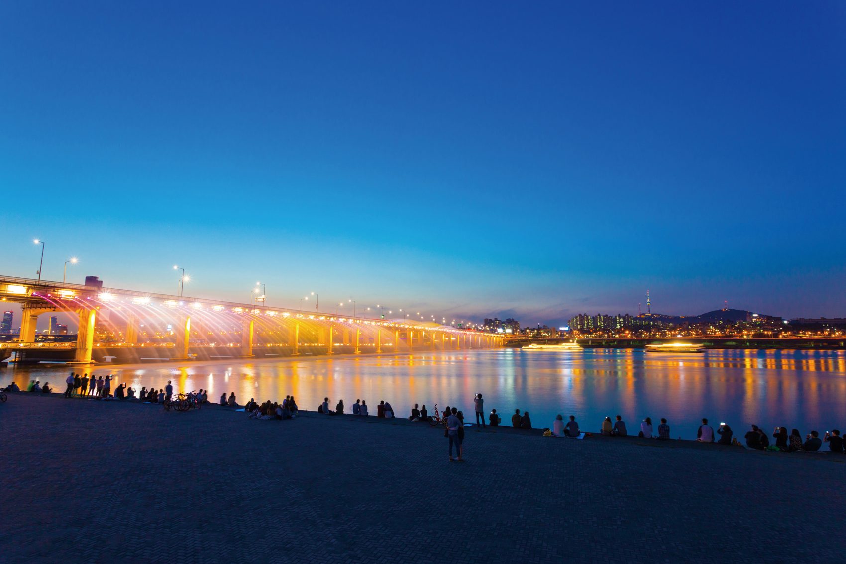 The fountains along Banpo Bridge in Seoul set off a nighttime light show as people watch on the side of the Han River.
