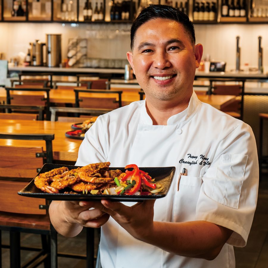 A smiling chef, Trong Nguyen, holding out a plate of crawfish at Crawfish & Noodles, Houston. 