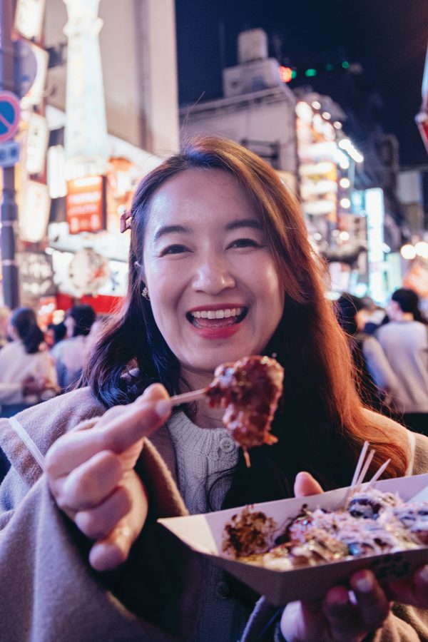 Woman holding up a takoyaki ball with a smile on her face