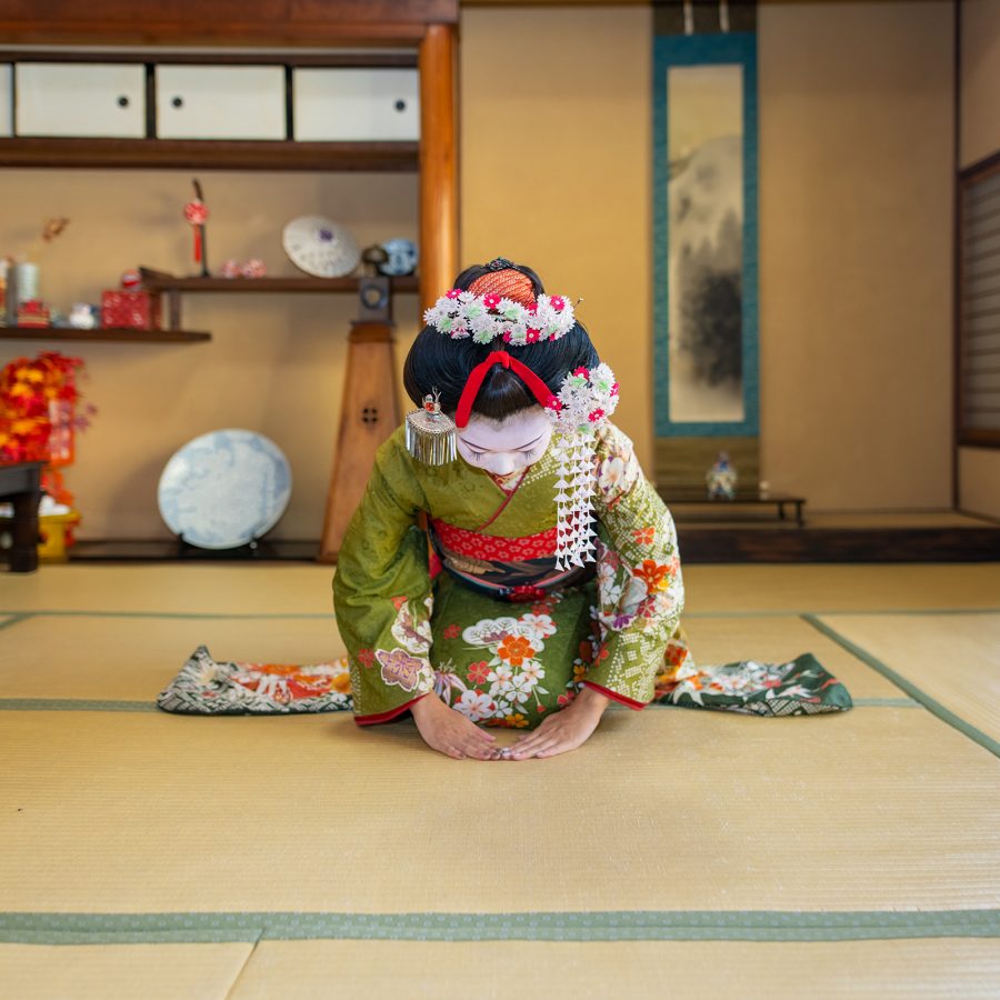 A geisha in full kimono and make up bowing on a bamboo mat in a traditional Japanese lodging in Kyoto.