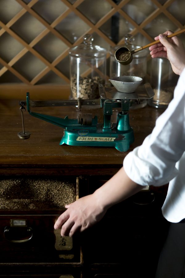 A person measuring dried tea leaves on a weight scale to make incense souvenirs in Kyoto.