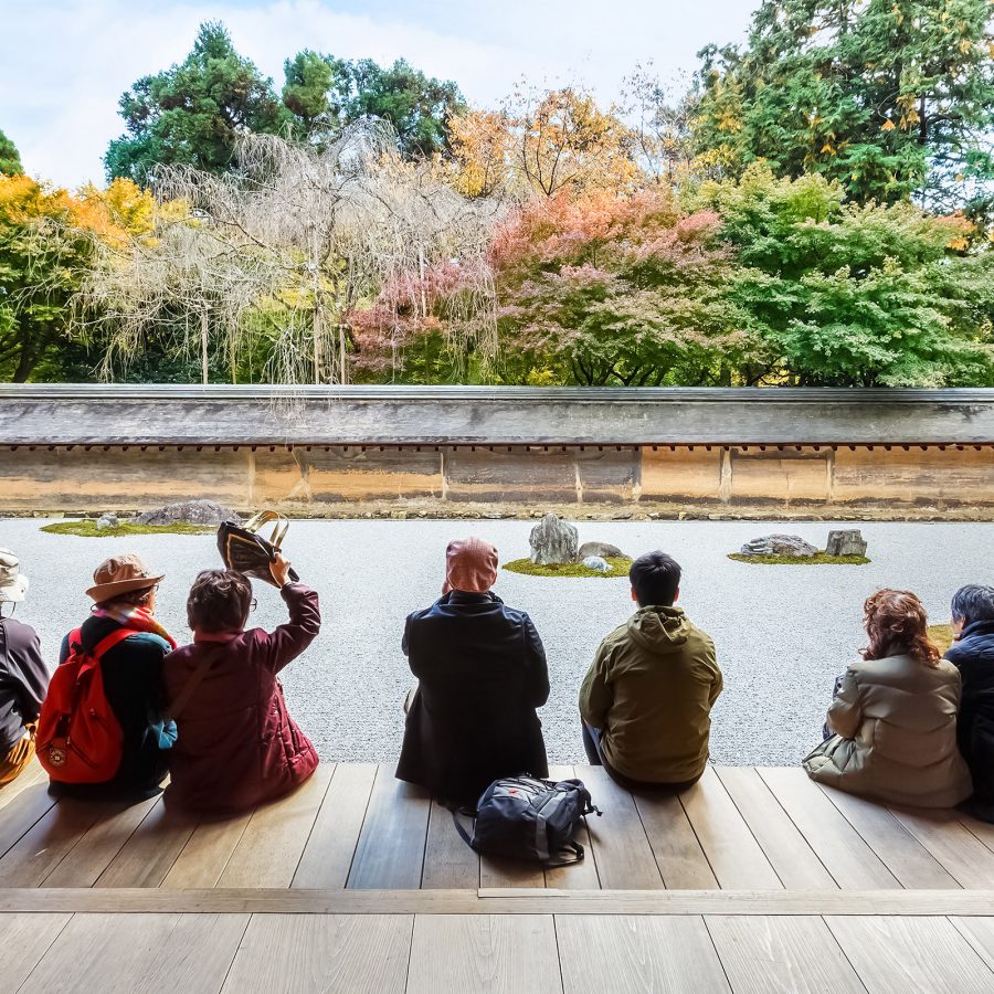 A group of travellers sitting while admiring the karesansui zen rock garden in Ryoan-ji in kyoto on a sunny day.