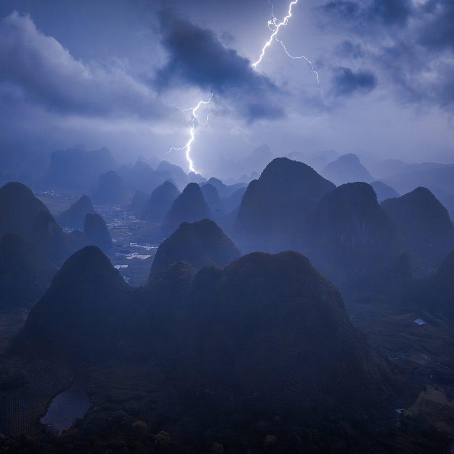 An image titled Wild Child Chasing Dreams in the Sky shot by Hong Kong photographer Kelvin Yuen depicts lightning bolt striking through the night sky over Guilin mountain range in China