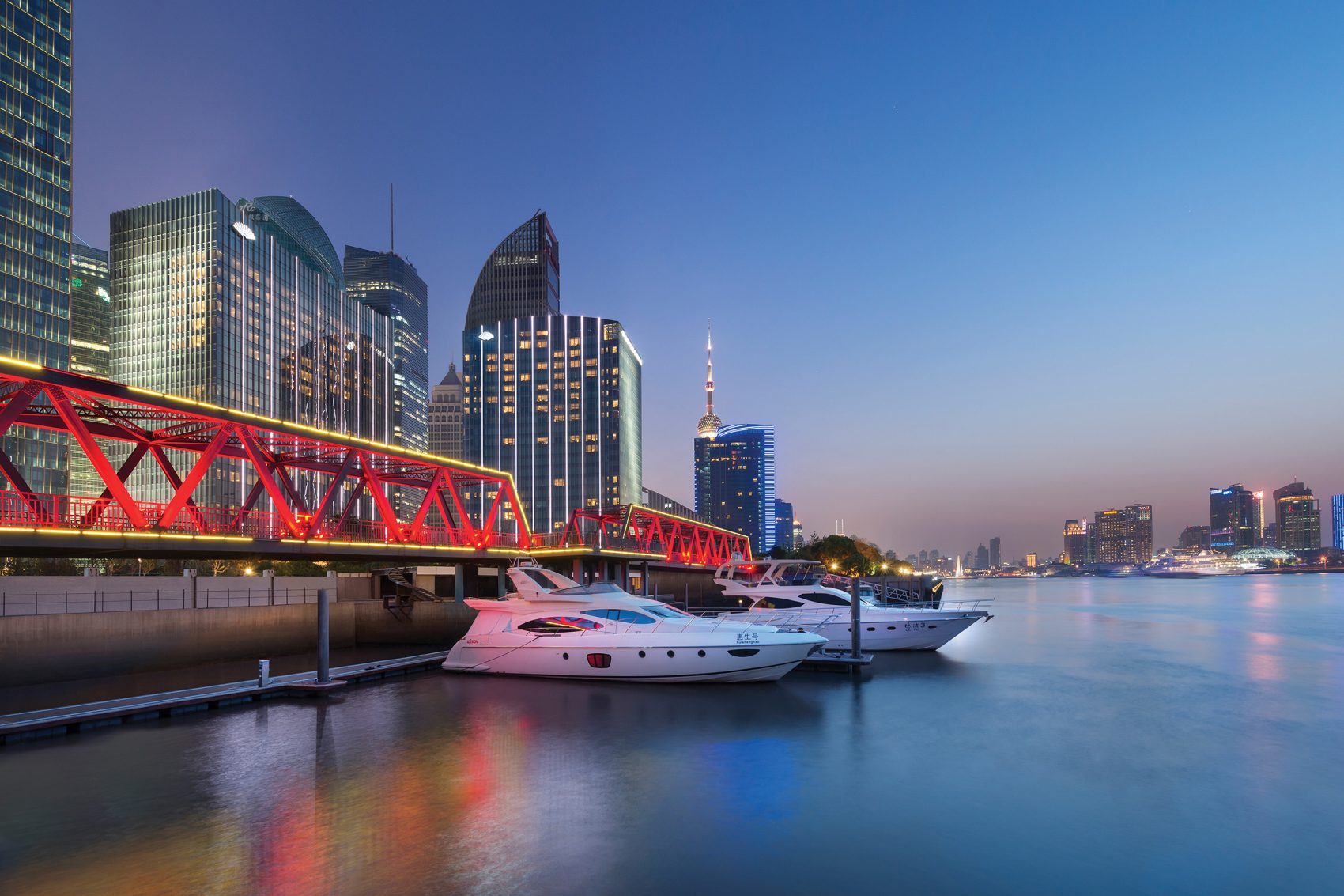 Shanghai’s skyline at night with boats in the water.