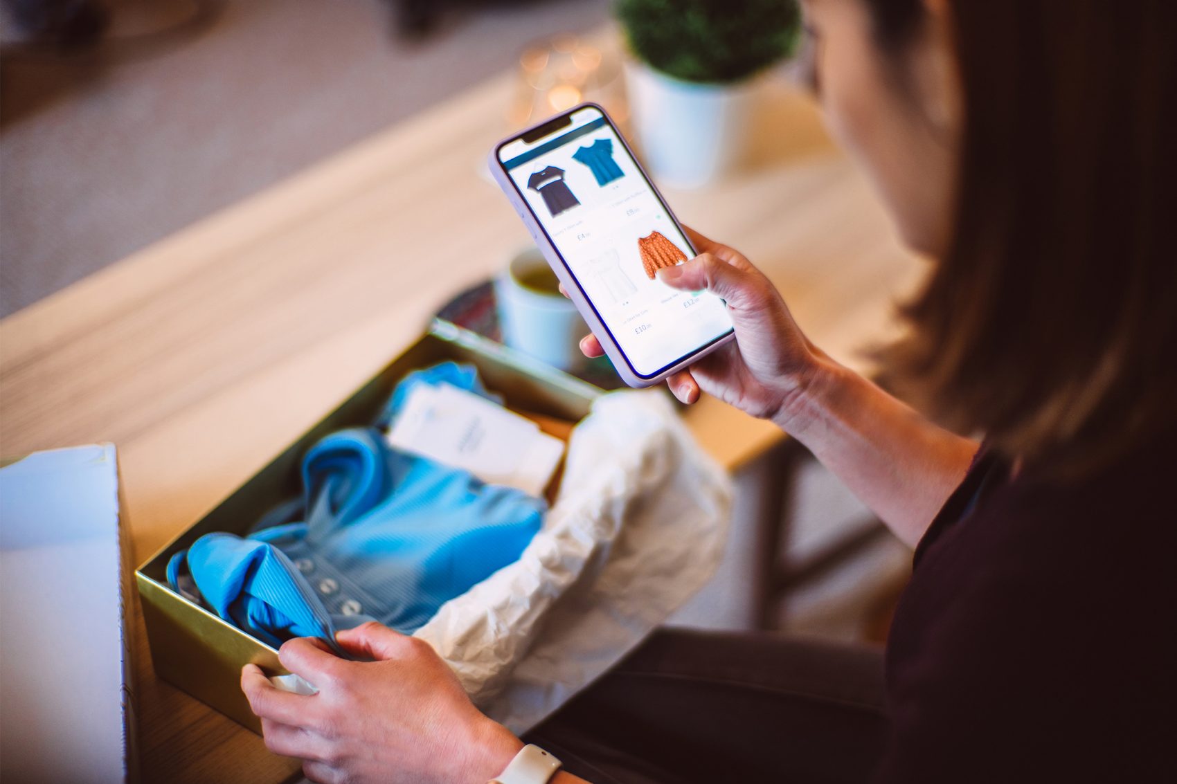 Woman unboxing an item of clothing with their phone in the other hand.