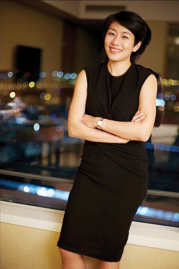 A portrait photo of Grace Vineyard owner and Chinese female winemaker Judy Chan, posing infront of a window with a view of the skyline.