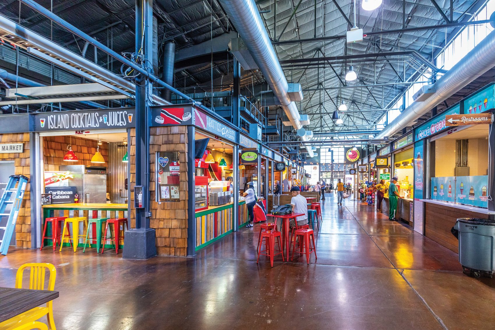 The interior of Dallas Farmers Market includes dozens of shopfronts along a wide aisle, while colourful chairs are placed in front of an eatery. 