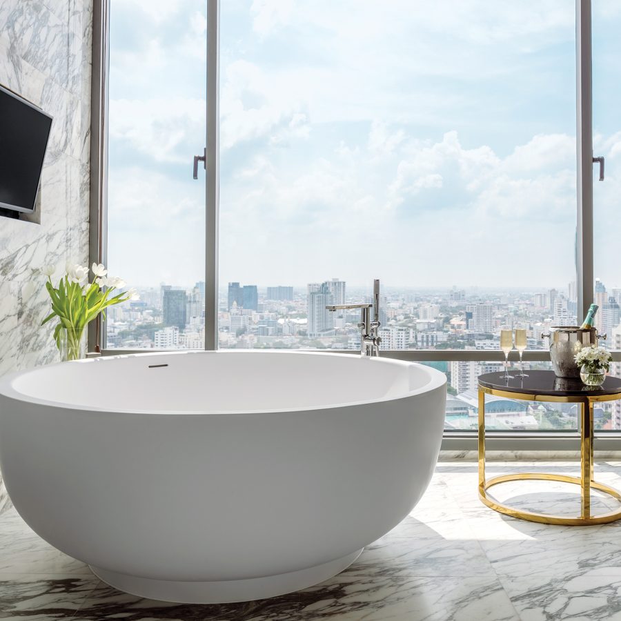 A room with a bath and TV inside 137 Pillars Suites & Residences, Bangkok looking outside into the city.