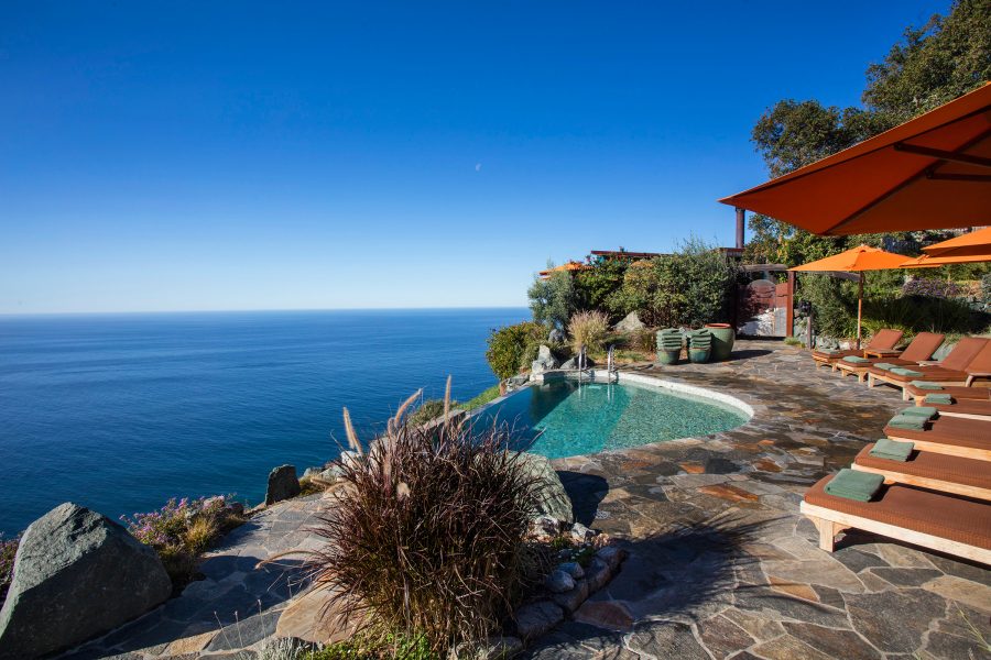 Pool shot with sunbeds and an umbrella fom Post Ranch Inn, California, USA, looking into the sea. 