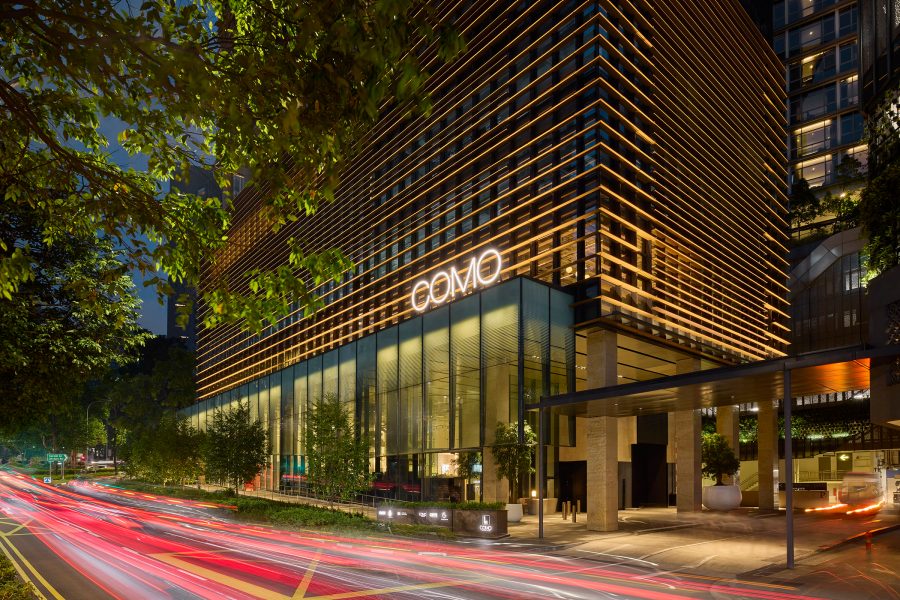 Exterior of Como Metropolitan Singapore hotel at night with streaks of red lights on road outside.