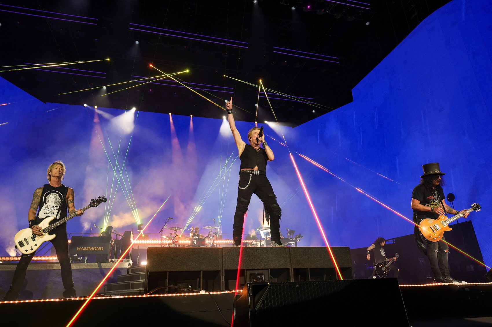 he members of Guns N’ Roses, who are on their 2025 world tour, perform as colourful spotlights illuminate the stage.