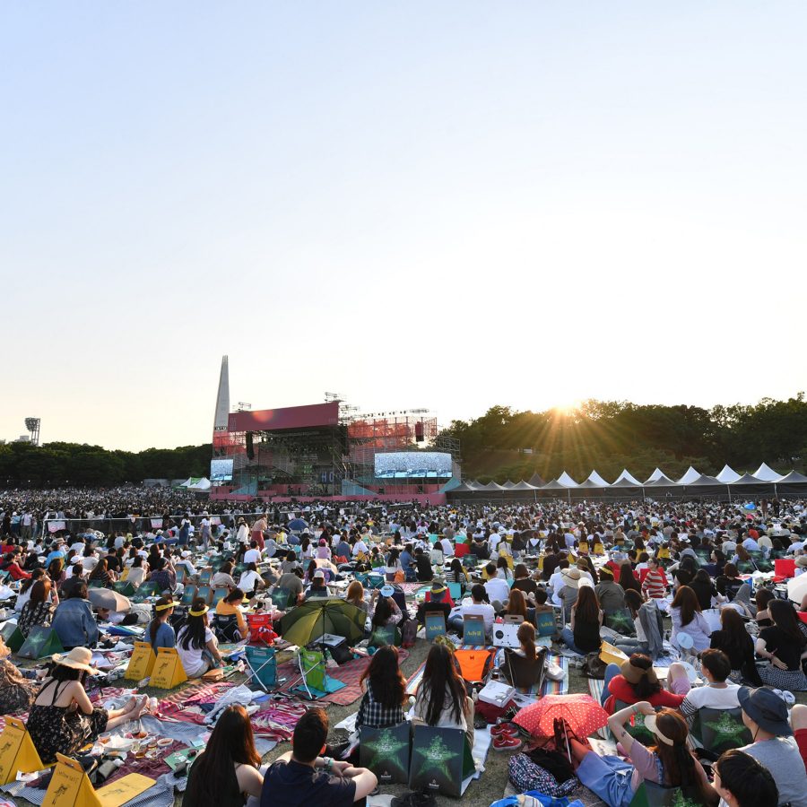 A crowd of people sitting on mats and towels waits in front of a stage at the Seoul Jazz Festival. 