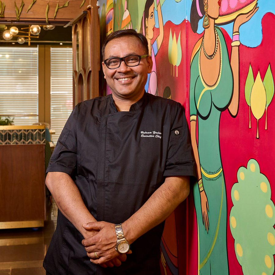 A profile shot of Chef Balram Yadav next to a vibrant wall art taken at Spice Bazaar in Hong Kong.