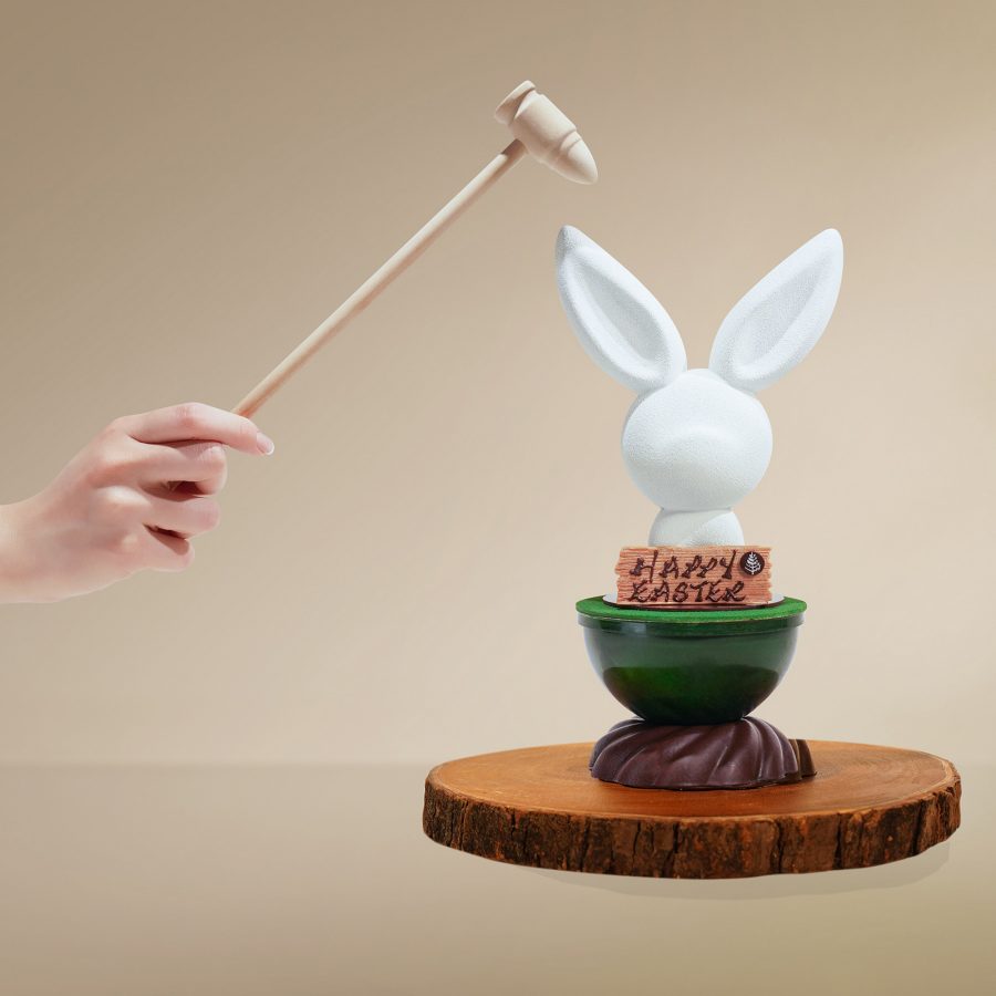 Person holding a small hammer over an Easter bunny-shaped dessert.