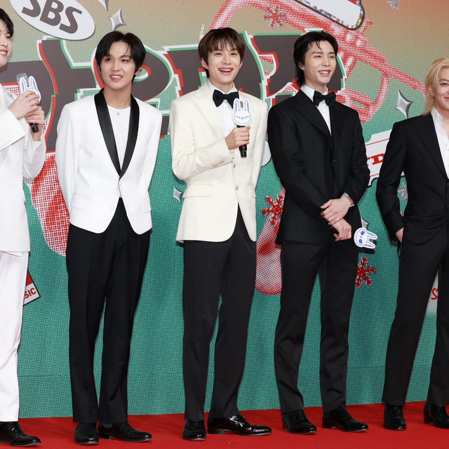 A red carpet photo of the six members of members of group NCT 127, dressed in black and white suits.