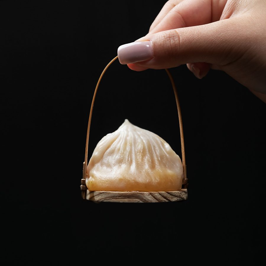 A hand holding a single xiaolong bao dumpling on a steel miniature basket served at The Refinery private member’s club.