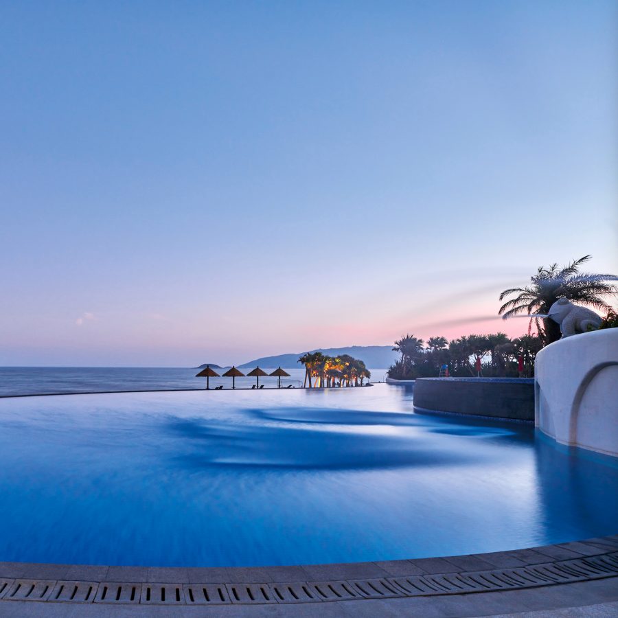 The outdoor pool at Dusit Thani Sandalwoods Resort Shuangyue Bay Resort appears to blend into the blue sea and sky in the evening. 