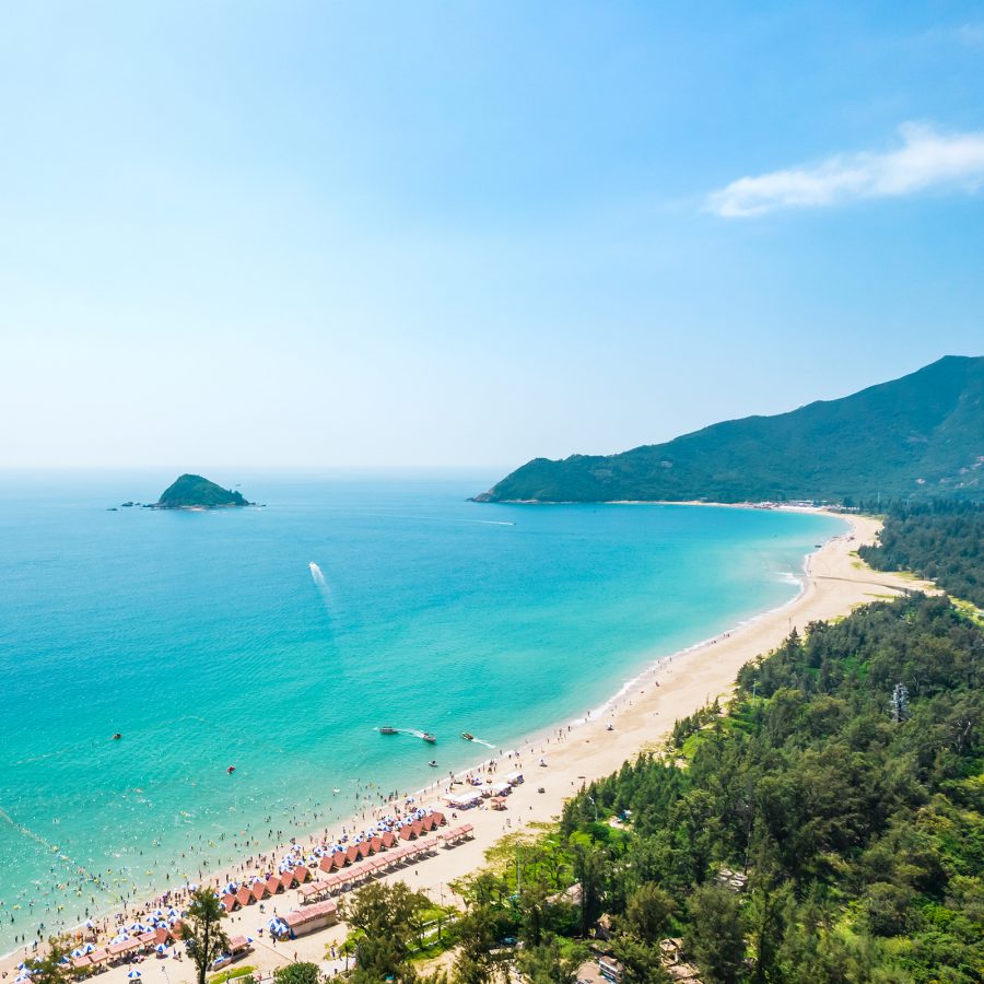 An aerial view of Xichong Beach, Shenzhen shows its long stretch of white sand straddled by lush forests and the aquamarine sea. 