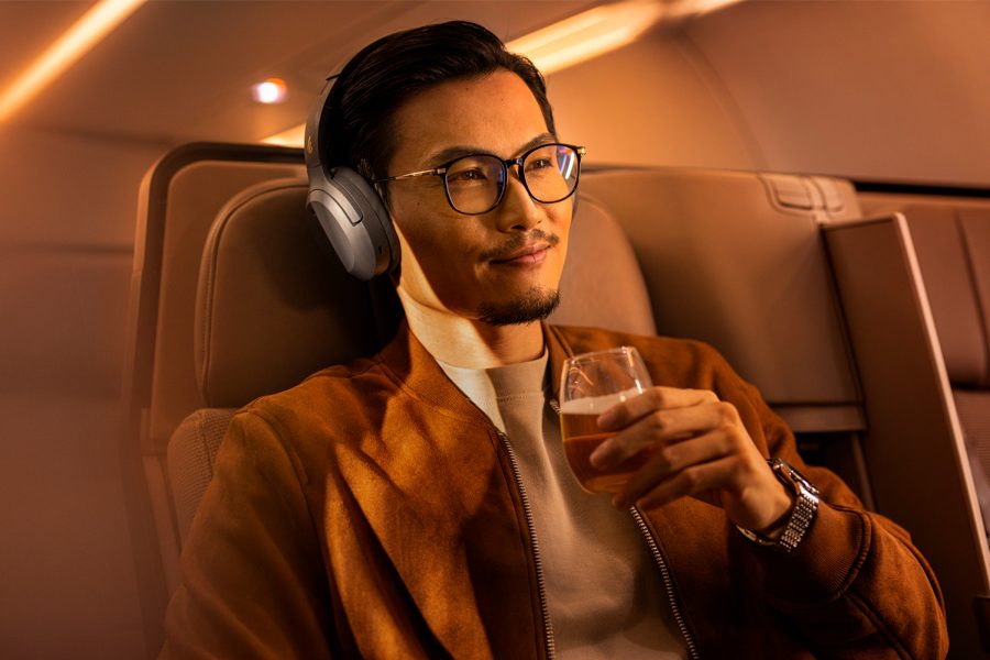 A man wearing glasses and headphones sipping champagne as he listens to headphones.