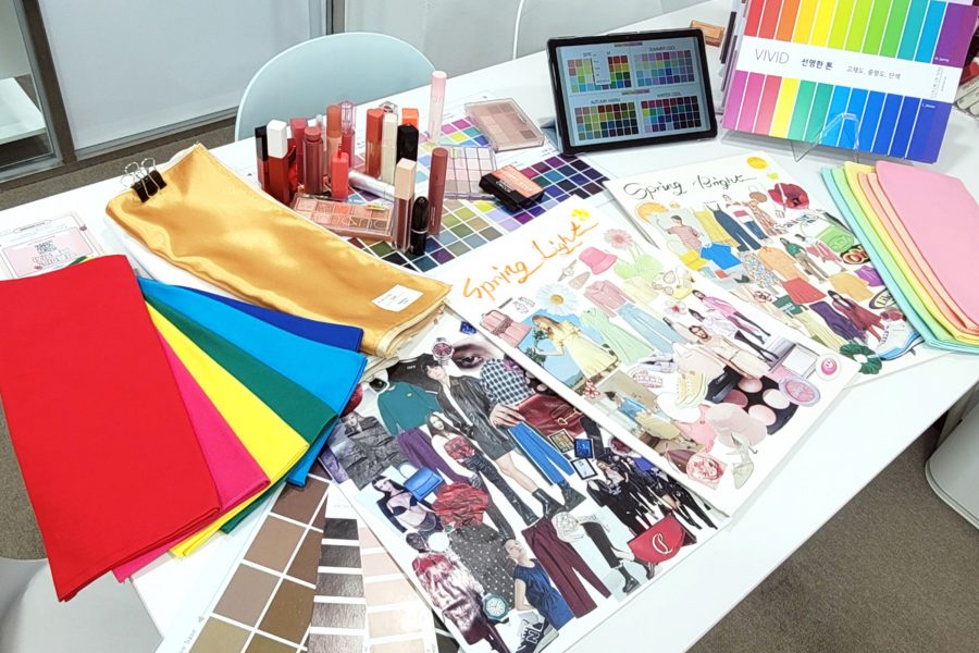 A table filled with personal colour analysis materials, including colour swatches, makeup products and a tablet. 