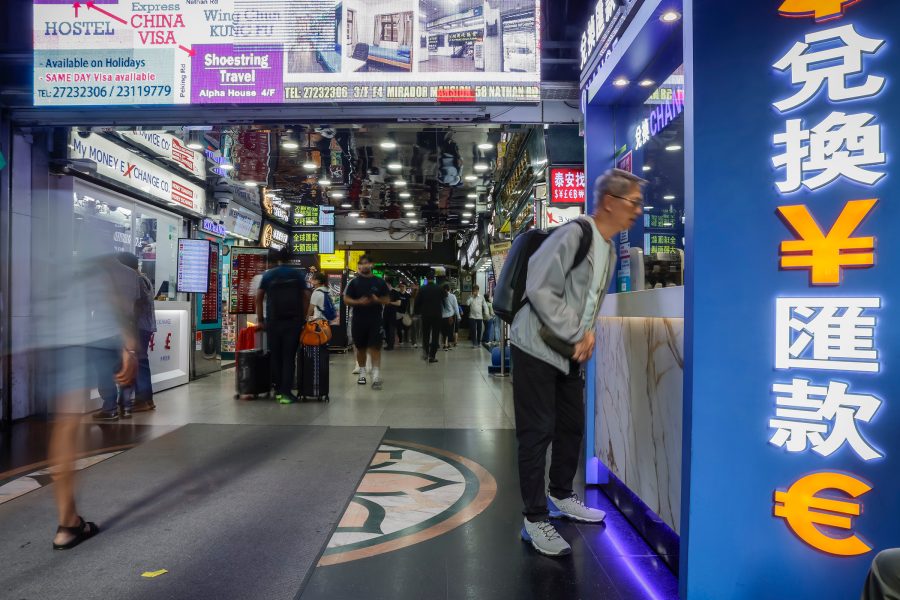 A man talking at a currency exchange stall while people walk by inside Chungking Mansions in Tsim Sha Tsui, Hong Kong.