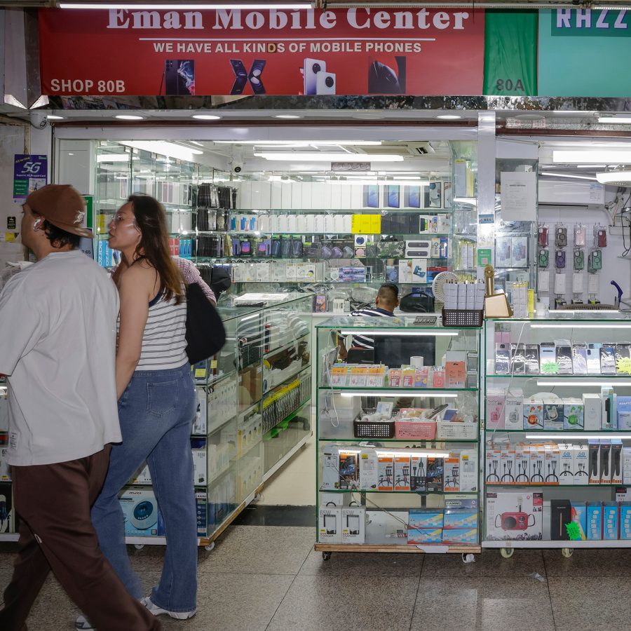 Two tourists walking by a shop selling mobile phones and electronics in Chungking Mansions in Tsim Sha Tsui, Hong Kong.